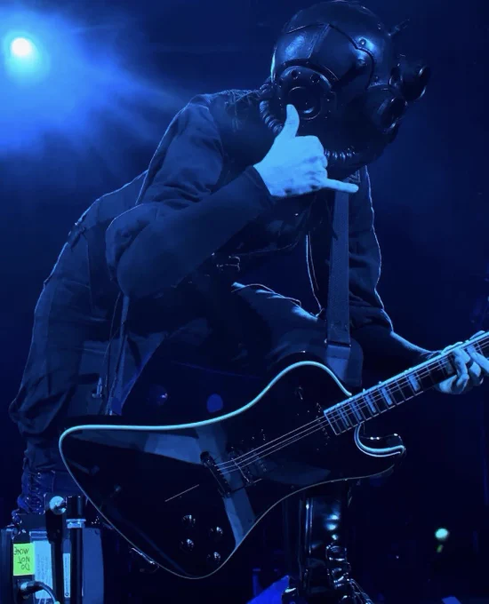 phantom ghoul leaning forward while playing guitar, his right hand is making a “phone” gesture, dark blue lighting