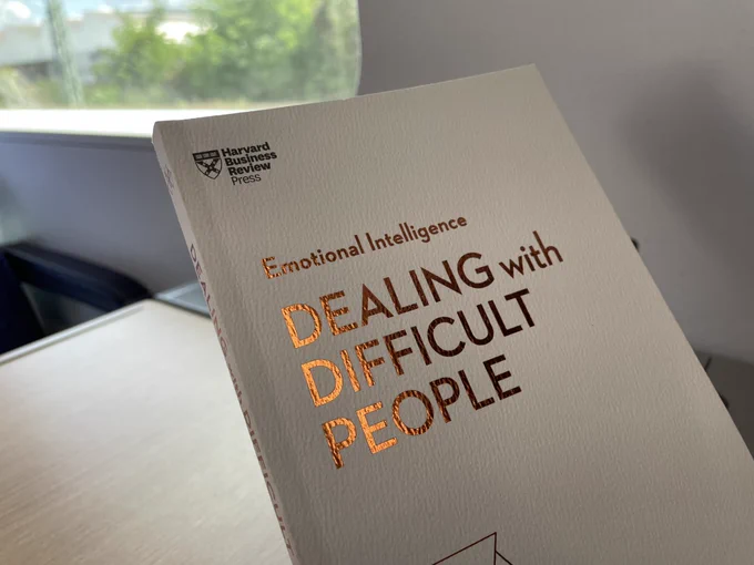 A book in front of a train window. The title reads: Emotional Intelligence. Dealing with difficult people