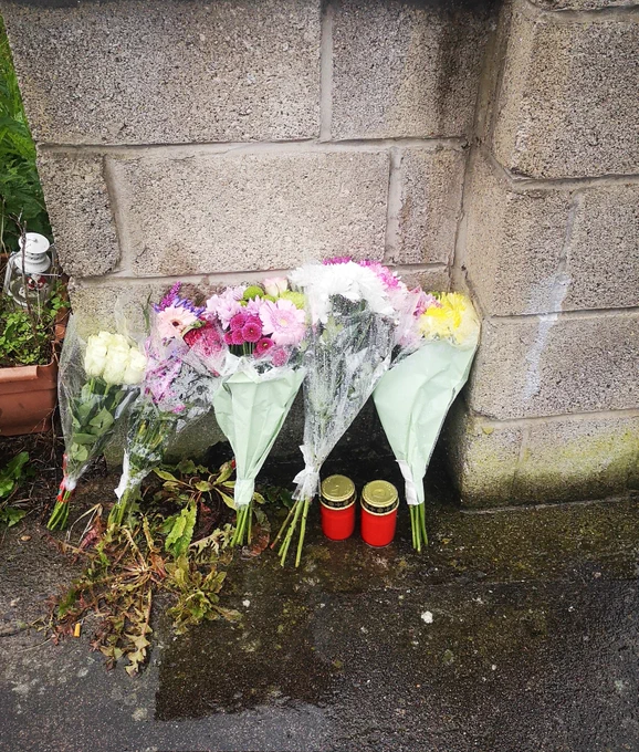 A number of bouquets with white roses, yellow chrysanthemums laid against the front garden wall of family home outside where Martin was attacked. 