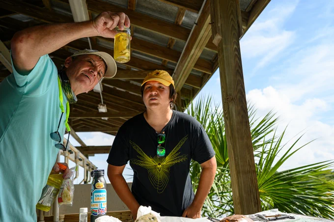 two people look up at a jar with unknown fluid in it while in a lab set up in an open pole barn