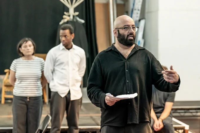 Aaron Neil holds script in rehearsals for A Mirror. Sara Houghton and Micheal Ward are on the background.