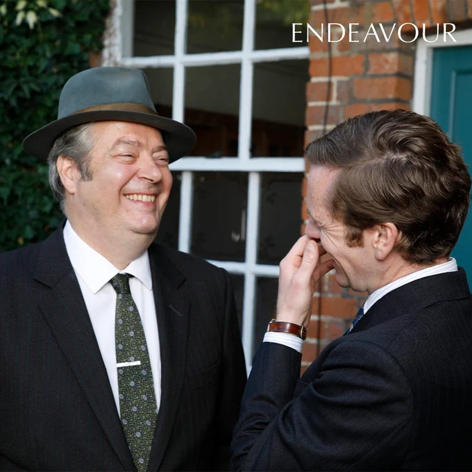 Endeavour Morse and Fred Thursday sharing a joke. They are facing each other with warm expressions on their faces.