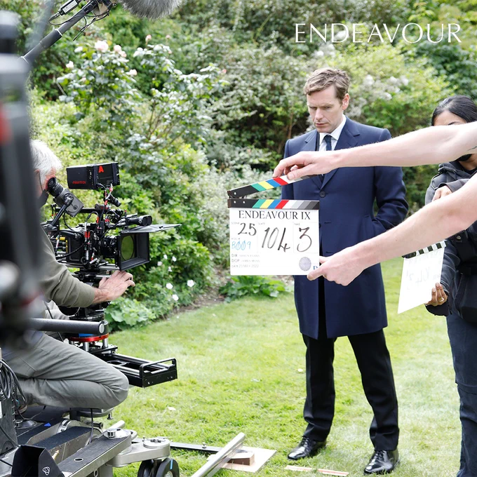Actor Shaun Evans, who plays Endeavour Morse, preparing to start a scene. He is stood behind a clapperboard that reads Scene 25, Slate 104, and Take 3. The cameraman is ready to commence filming.