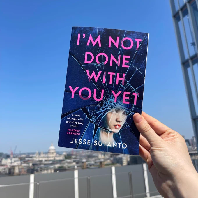 Hand holding a copy of I'm Not Done With You Yet by Jesse Sutanto up against a clear blue sky