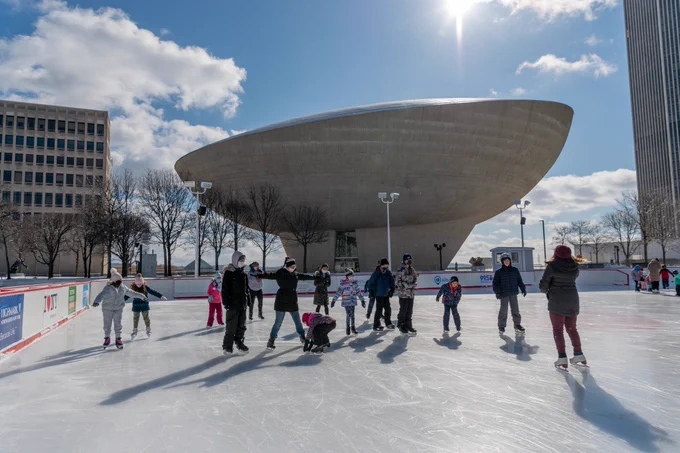 Photo of the Empire State Plaza ice rink with the Egg Performing Arts Center in the background and people skating in the foreground. 