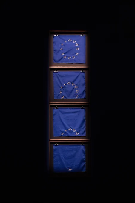 An image of a multimedia sculpture (© copyright Enrique Ramirez), depicting a series of EU flags (but with small boats in place of stars) seeming to sink below a horizon.