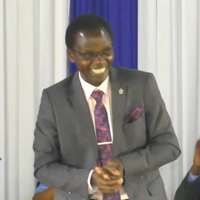 Elder Richard Mutai smiles as he preaches the sermon in Kenyan Sign Language for Possibility Ministries Sabbath 2023 at the Seventh-day Adventist Church in Kariobangi, Kenya.  He is wearing a grey suit with a white shirt and a purple & pink tie and pocket scarf.