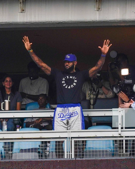 LeBron James waves to the crowd at Dodger Stadium. He wears an Uninterrupted t-shirt with Dodgers shorts.