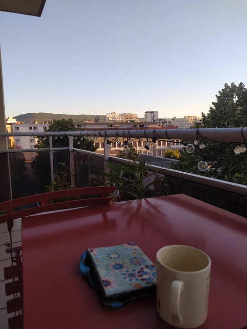 Liseuse et tasse posées sur une table de balcon, lumière du soleil levant. 