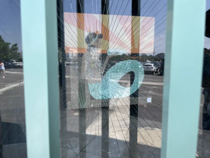A confusing “arty” image taken through broken glass with blue poles on the left and right in the foreground, and looking through the spider web of broken glass you can see some kind of art that looks like a colorful mermaid.