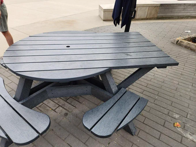 A circular PVC picnic table with one part with a rectangular jut-out that lacks a bench.