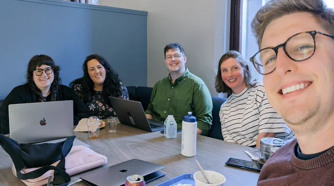 Selfie of four people sitting around a table with lunch and computers. 