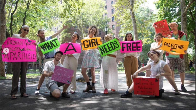 A group of people hold colorful signs that read, "What a girl needs: Free Palestine".