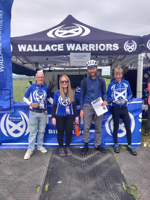 A blue gazebo tent with 'wallace warriors' written on it. Four people in blue cycling jerseys look at the camera.