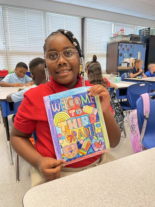A student holds up a sign that says “Welcome to Third Grade.”