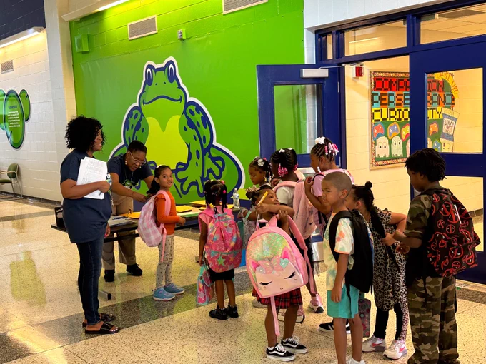 Two staff members help students in the school hallway.