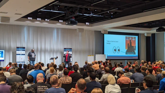 Two people at a conference stage in front of multiple people 