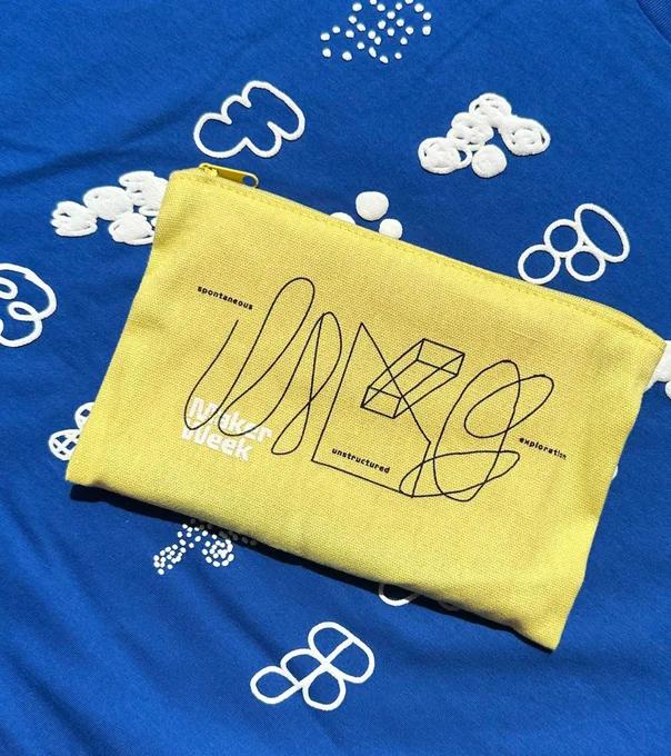 yellow hand bag with scribbes and Maker Week in white again royal blue tshirt with multiple white figma logos