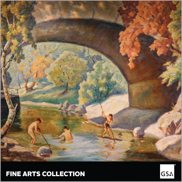 Boys playing in a river under a bridge with big tan rocks on the right side and a small tree with a few branches that are full of leaves.  there are also branches from a reddish tree and several green trees and grass in the background.