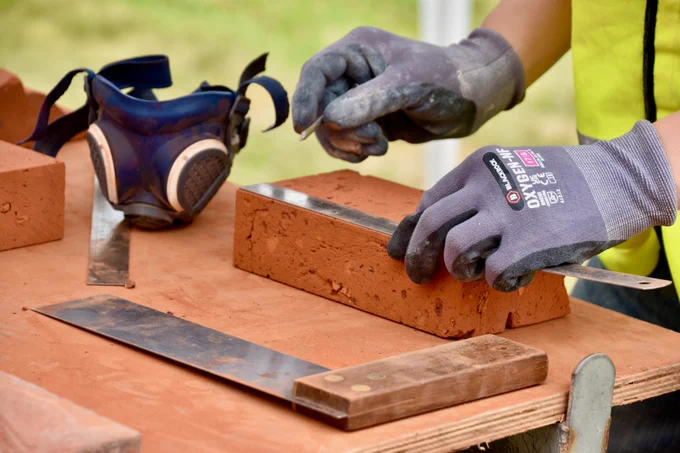 A craftsperson measuring a brick on a workbench surrounded by tools