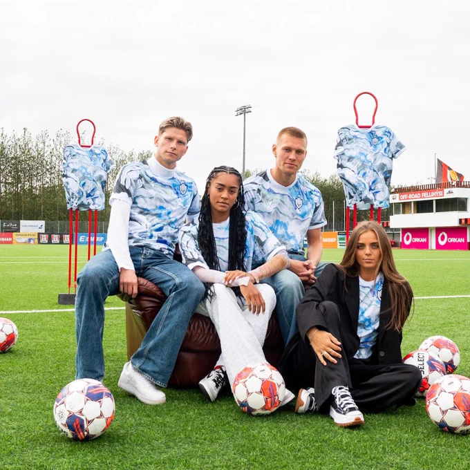 Models wearing the shirt sat on the pitch at Vikingur’s home stadium, three are sat on a chair with one on the floor. There are footballs on the pitch nearby and two free kick mannequins, with the shirts draped over them