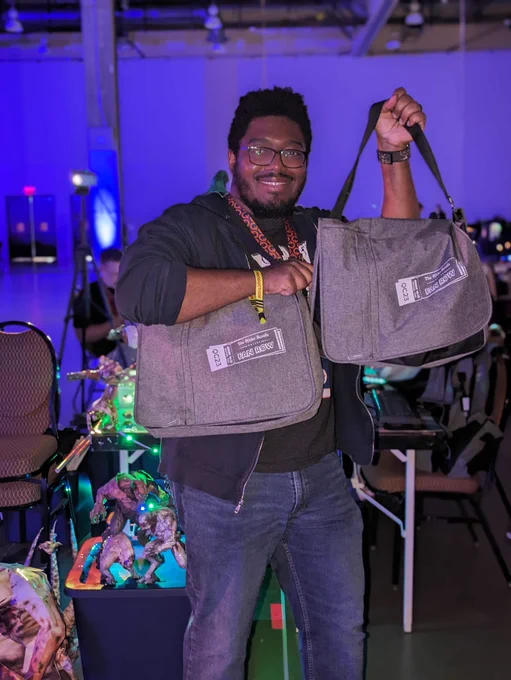 ESO Community Manager, Kevin Gbolie, holds up two ESO x QuakeCon BYOC Survival Kits in front of the ESO Fan Row.