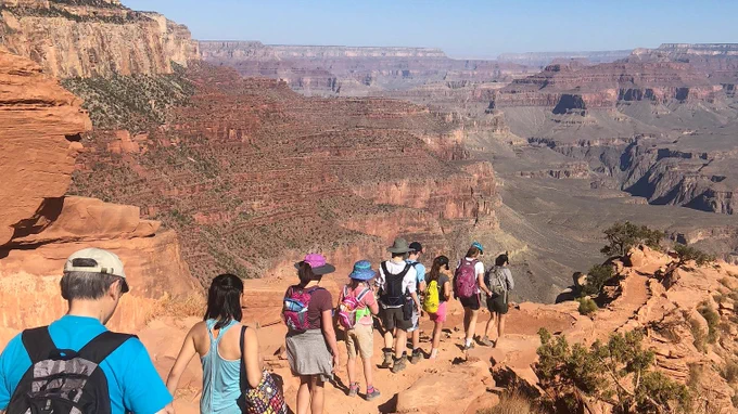 A line of visitors descends a dirt trail into the Grand Canyon
