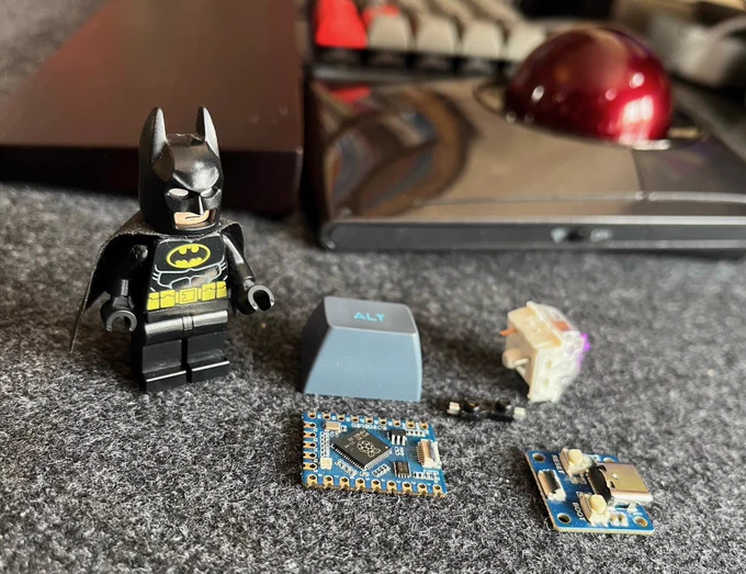 a picture of the waveshare rp2040-tiny microcontroller and usb boards, a kailh hotswap socket, a key switch, a blue alt keycap, and a batman lego minifigure for scale