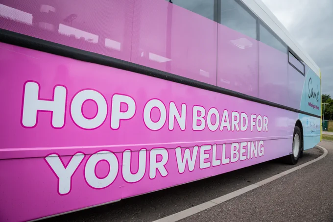 Image of the side of the pink WoW bus, which reads 'Hop on board for your wellbeing'. 