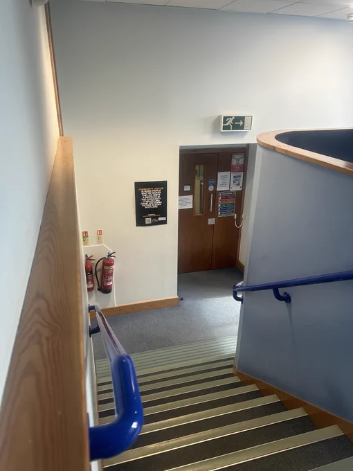 Perspective from the top of a flight of stairs. There is a poster on the wall at the bottom of the stairs that reads 'Community justice is when people who have broken the law serve a sentence in the community. It means less crime and fewer victims across Scotland'