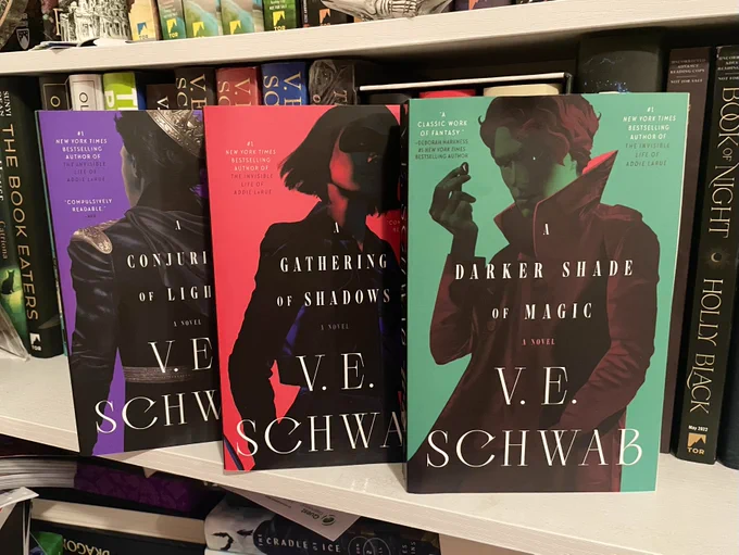 A Darker Shade of Magic, A Gathering of Shadows, and A Conjuring of Light lined up on a book shelf. These are the new paperback repackagings 
