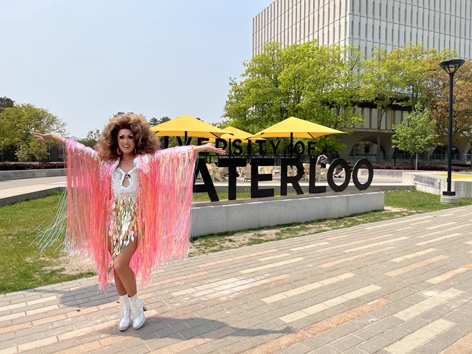 Kyne Santos stands in front of the University of Waterloo sign in the centre of campus on a sunny day .