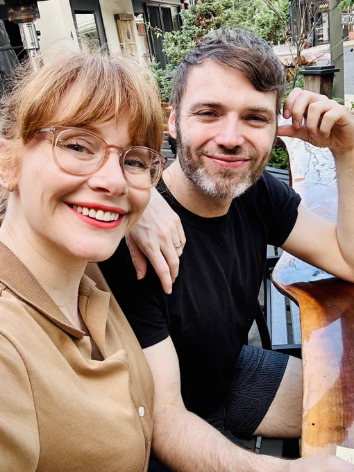 A profile selfie of BDH (left) and Seth (right) sitting at a wooden communal-style table for dinner.