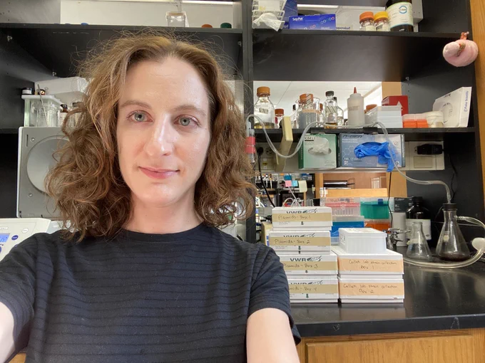 Selfie of Sierra looking tired in front of her work bench. Boxes of DNA and yeast strains are behind her, ready for her new lab.