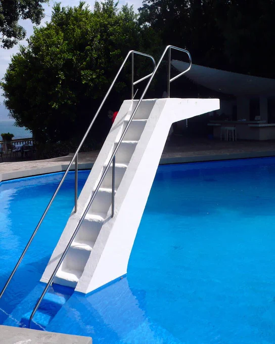 Blue pool with white steps leading to a diving board.