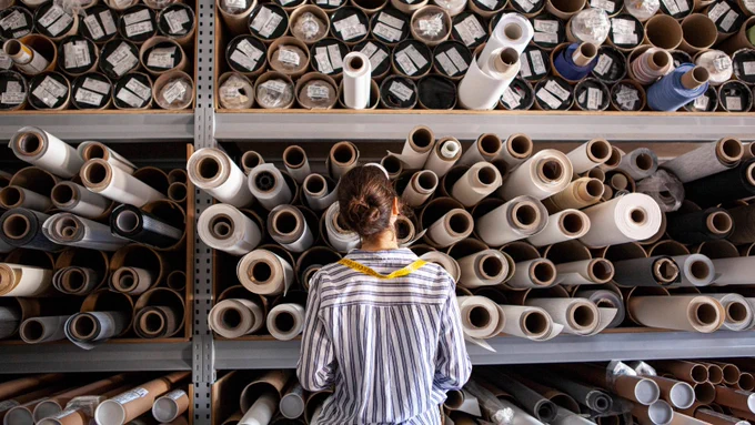 Portrait of textile designer choosing fabric from stack of rolls inside sustainable workshop