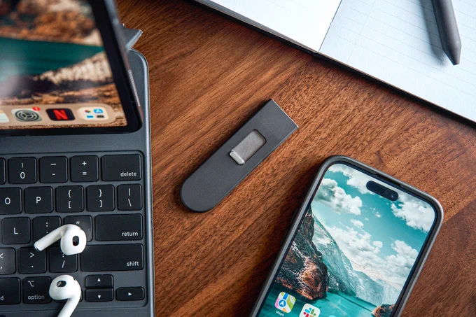 A Keen utility blade laying closed on a desk next to an iPad and iPhone.