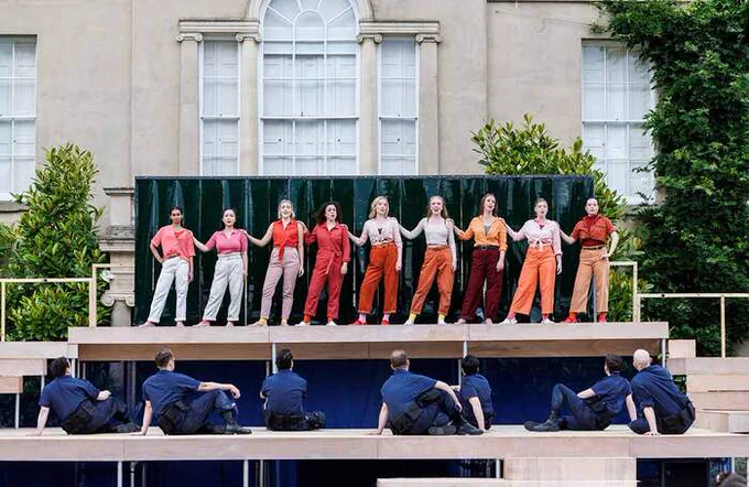 A row of performers onstage holding each others shoulders with one foot out to their side