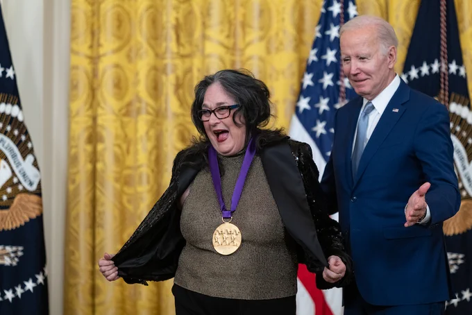 Judy Baca opens her jacket to show off her Medal of Arts while standing next to President Biden