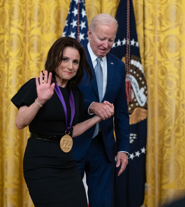 President Biden escorts Julia Louis Dreyfuss from the podium after bestowing the National Medal of Arts