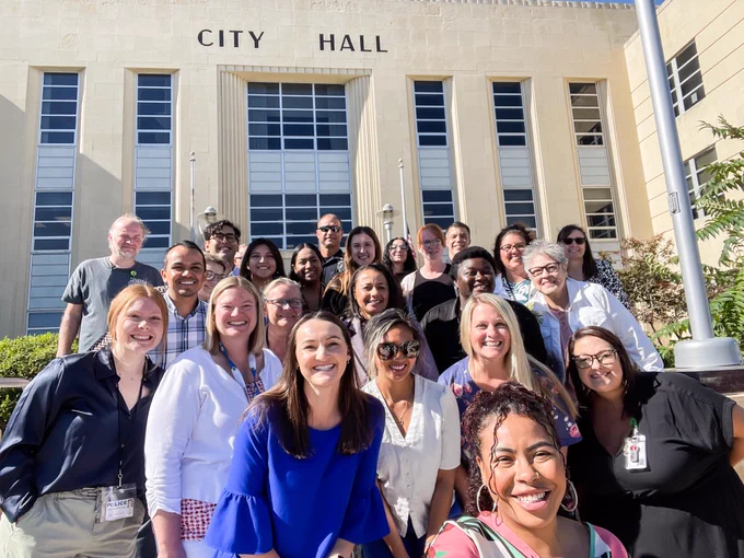 A group of employees smiling in front of City Hall.