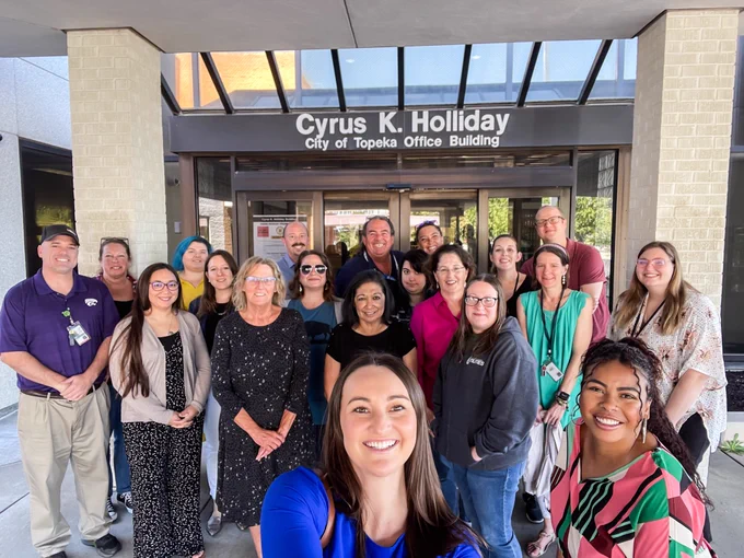 A group of employees smiling in front of the Cyrus K. Holliday Building.