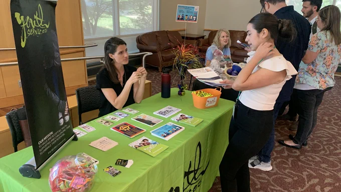 A student speaks with a representative from Youth Services behind a gree tablecloth clad table.