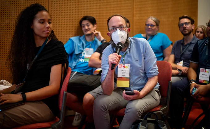 Participants at #BOSC2023, with a masked Michael Crusoe holding the mic to ask a question.