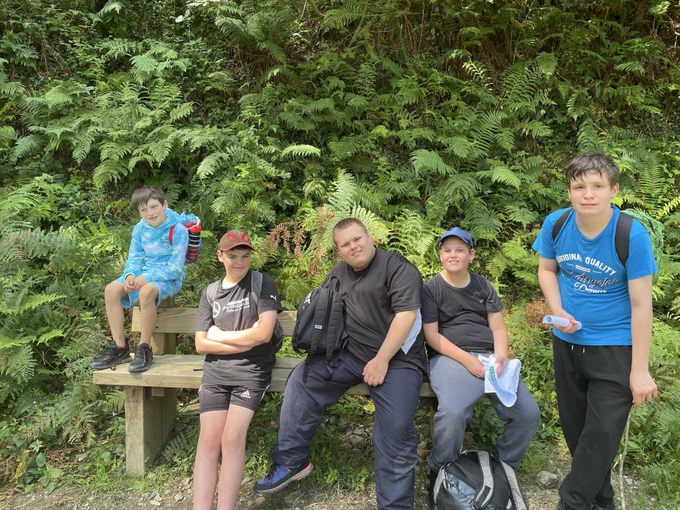 Five young men/boys sat on and around a bench at Cardinham Woods
