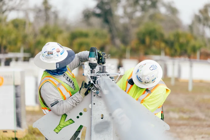 Two individuals in hard hats and high visibility vest installing solar trackers  