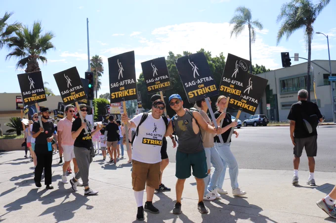 Many members walk and pose on the SAG-AFTRA strike picket line while holding SAG-AFTRA on strike signs