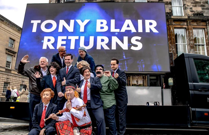 The cast of Tony! stand in front of a digi-van which has a large screen which reads 'Tony Blair returns' They are on the royal mile.
