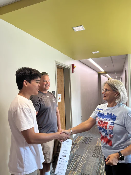 Provost and Executive Vice Chancellor Barbara Bichelmeyer shakes the hand of an incoming student while a smiling parent looks on. They are standing in the hallway of a residence hall on the University of Kansas campus.