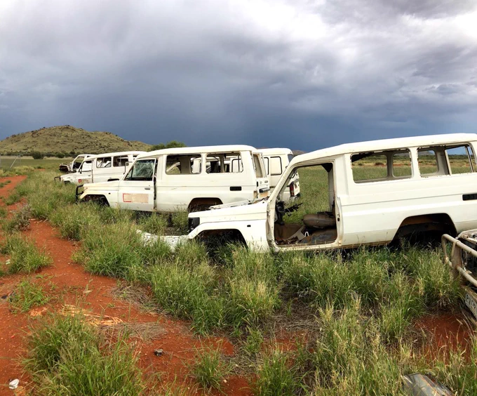 Three white abandoned vehicles in a green field.